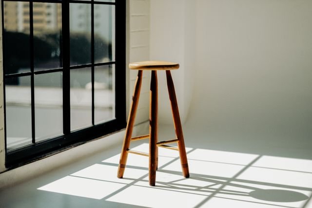 A minimalistic scene with a wooden stool bathed in sunlight next to a window.