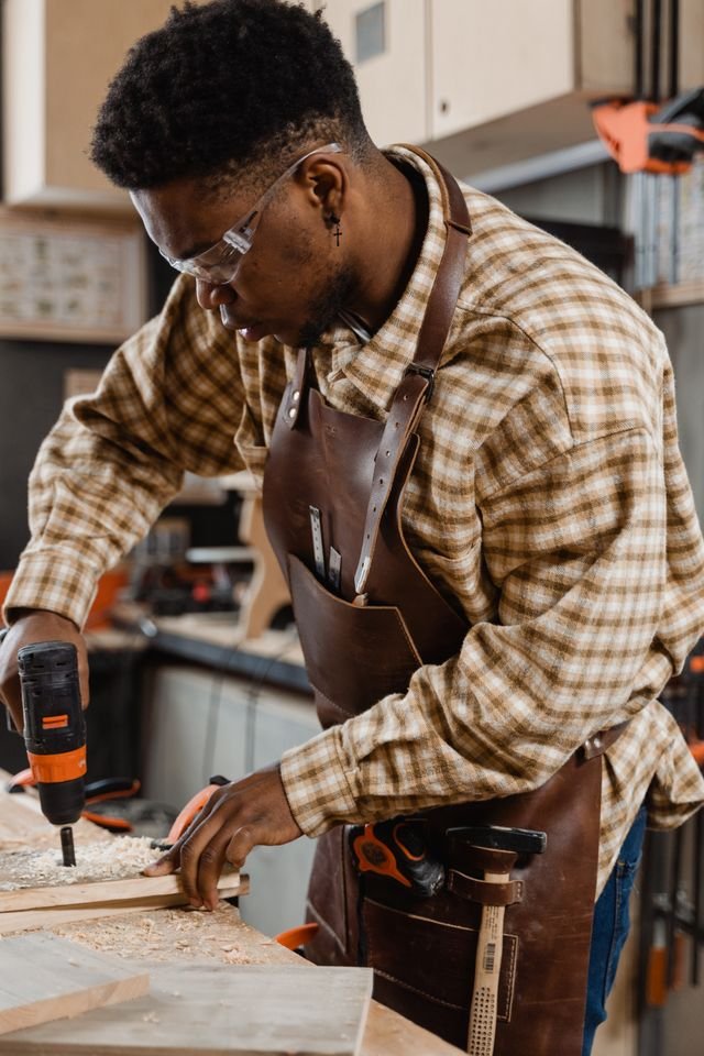 Focused woodworker in plaid shirt using a drill in his workshop. Captures the essence of craftsmanship.